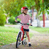 Una niña con casco rojo y camisa a rayas monta una bicicleta roja al aire libre.