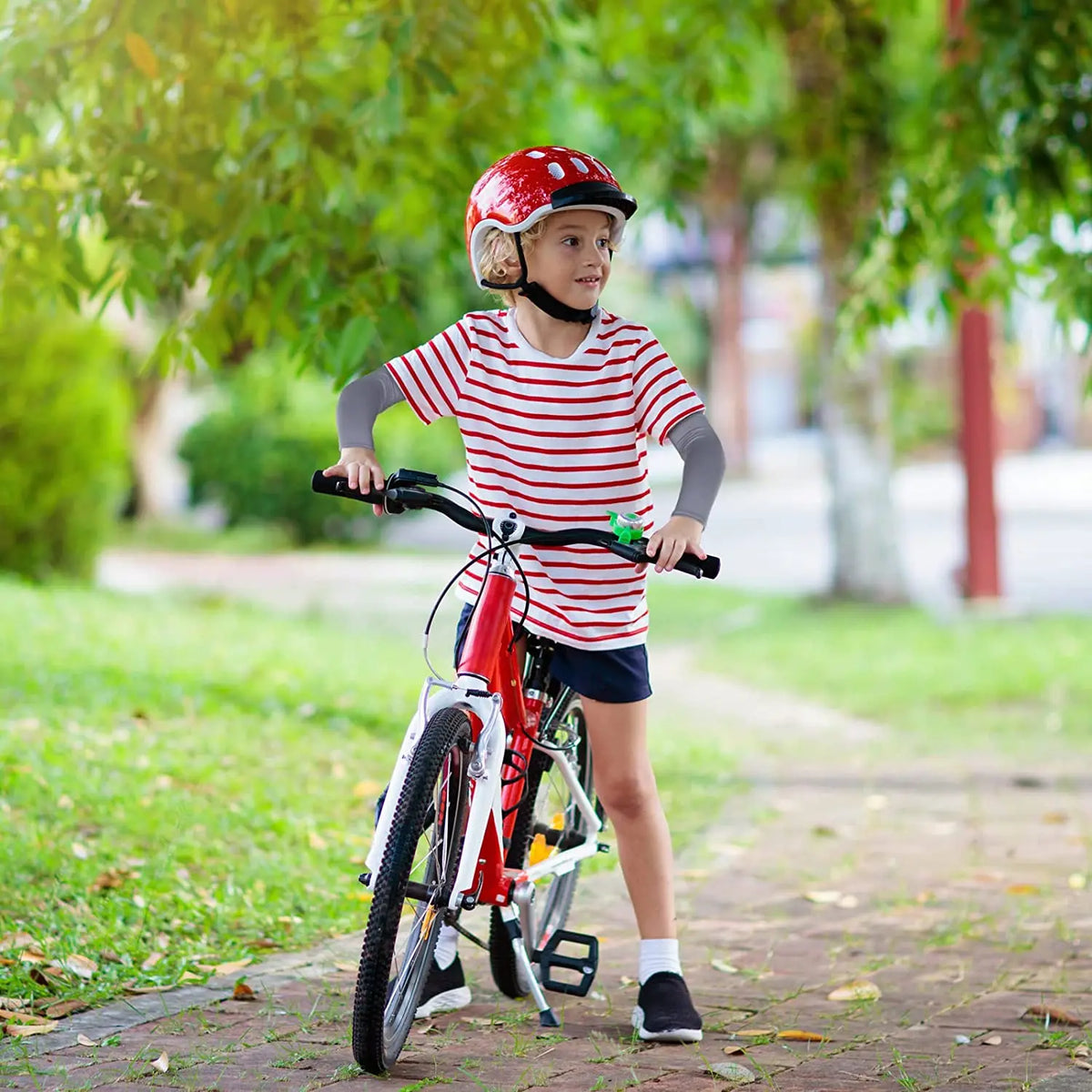 Una niña con casco rojo y camisa a rayas monta una bicicleta roja al aire libre.