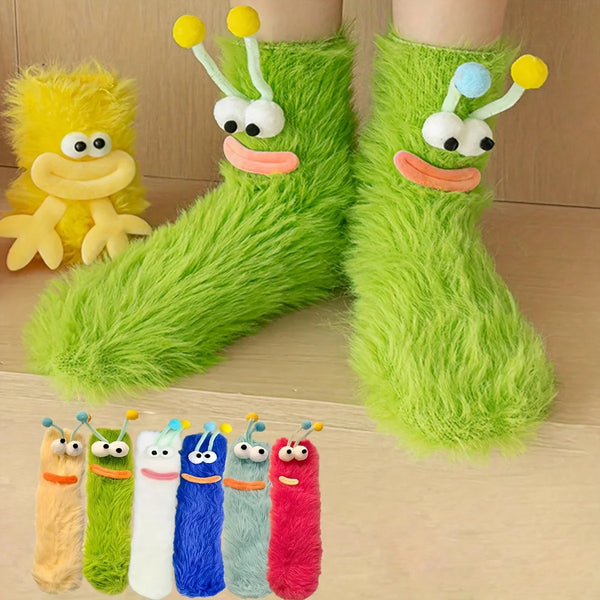A pair of bright green plush caterpillar floor socks with embroidered faces and a yellow plush toy in the background.