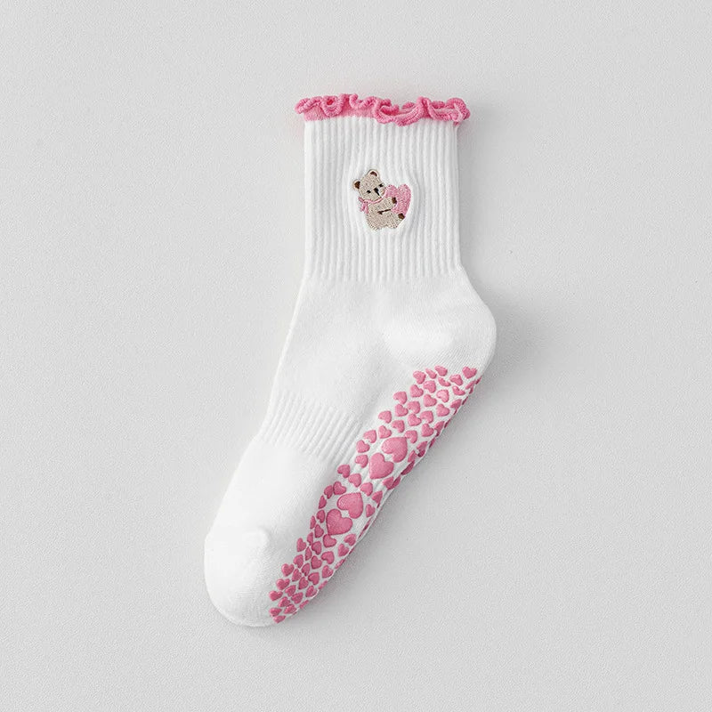Chaussettes de yoga blanches avec des bords froncés roses et un petit motif animal brodé.