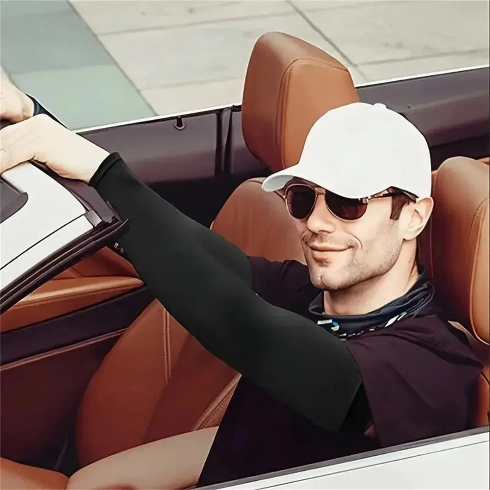 A man wearing sunglasses and a white cap is sitting in a car, wearing black compression arm sleeves.