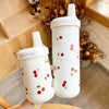 Un tumbler isotherme blanc avec un couvercle à paille décoré de petites illustrations de cerises rouges, présenté dans un env