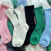 A variety of elegant embroidered cotton socks in pink, white, black, and green are displayed in clear plastic packaging.