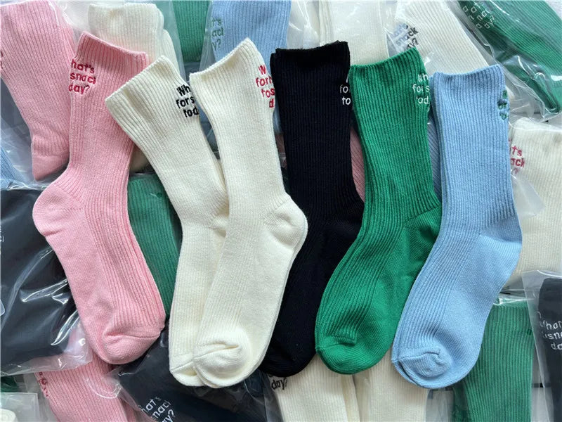 A variety of elegant embroidered cotton socks in pink, white, black, and green are displayed in clear plastic packaging.