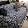 A plush sofa covered in a leopard print fabric, featuring various pillows and a small tray with a cup.