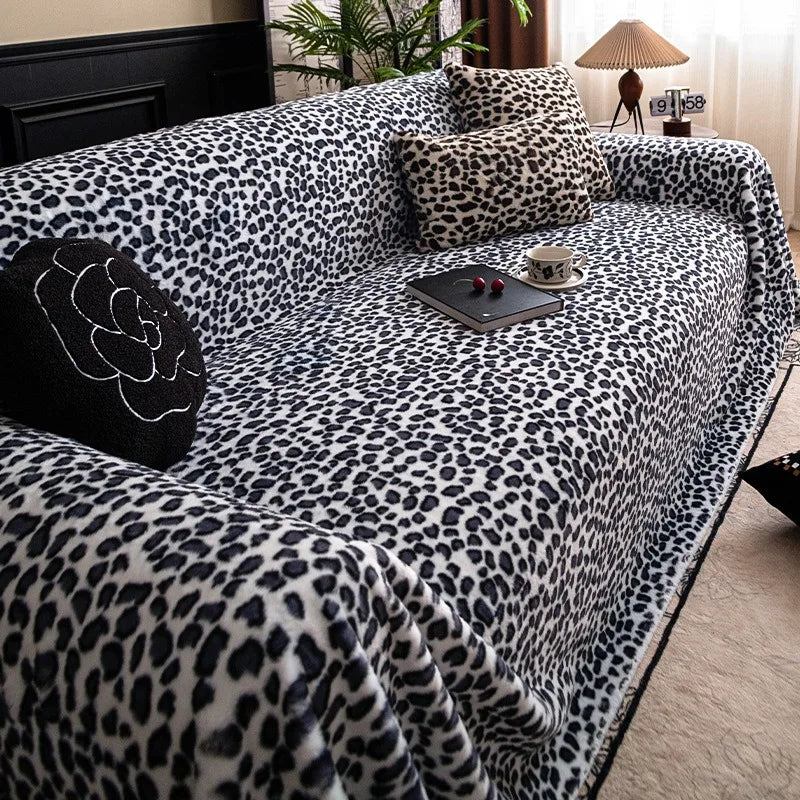A plush sofa covered in a leopard print fabric, featuring various pillows and a small tray with a cup.