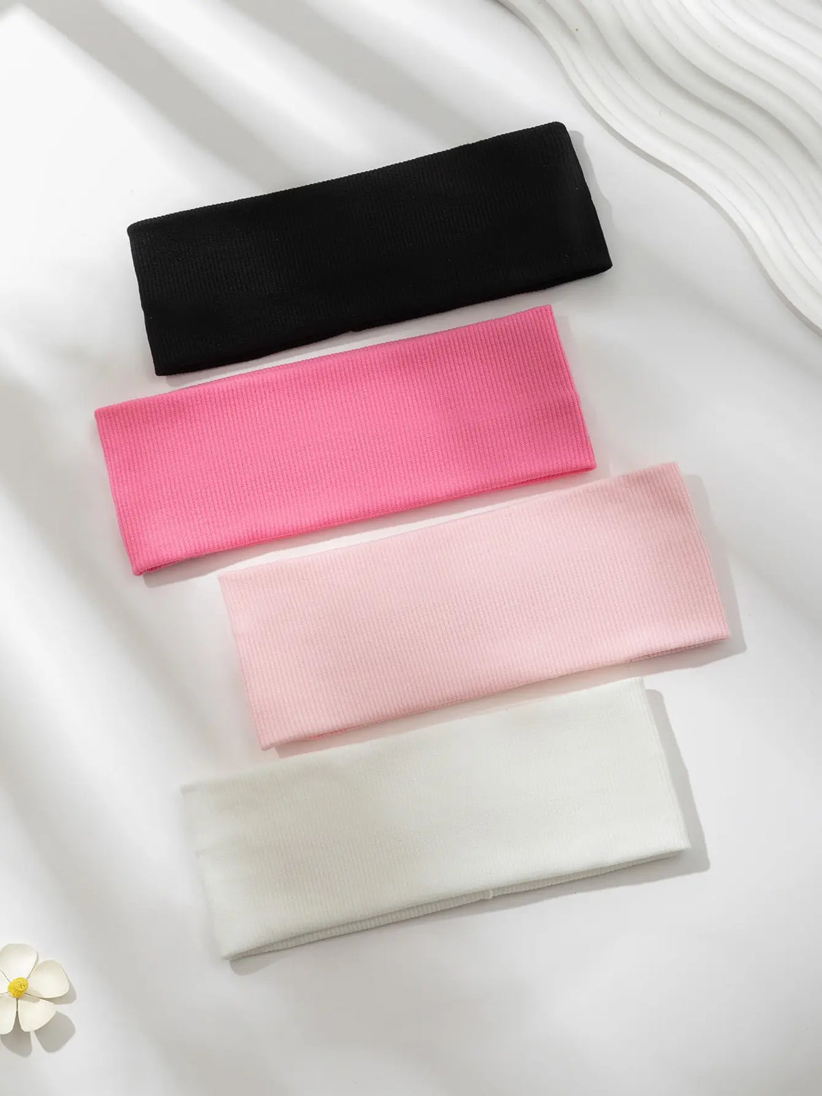 Un paquete de cuatro bandas elásticas para el cabello en negro, rosa y blanco exhibidas sobre un fondo blanco.