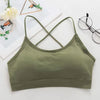 Olive green women's cross strap sports bra laid flat on a white background with glasses and greenery.