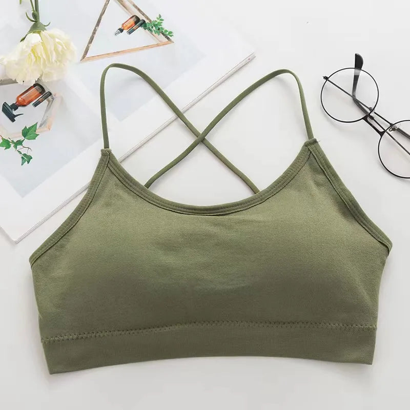 Olive green women's cross strap sports bra laid flat on a white background with glasses and greenery.