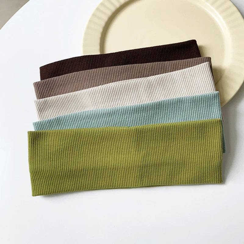 A stack of five colored elastic hairbands for fitness and yoga, including shades of brown, beige, gray, blue-green, and olive