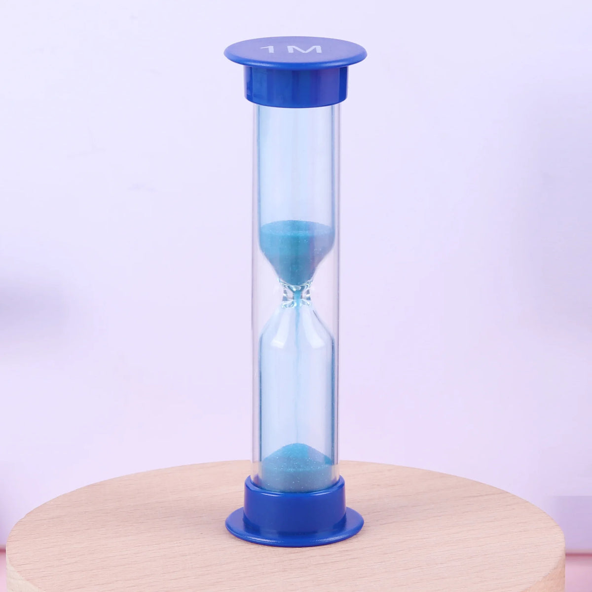 A tall blue hourglass with a clear glass body and a blue lid, resting on a wooden surface.