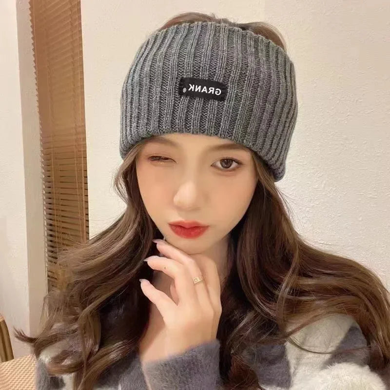 A woman models a grey knitted headband with black text on it against a light background.