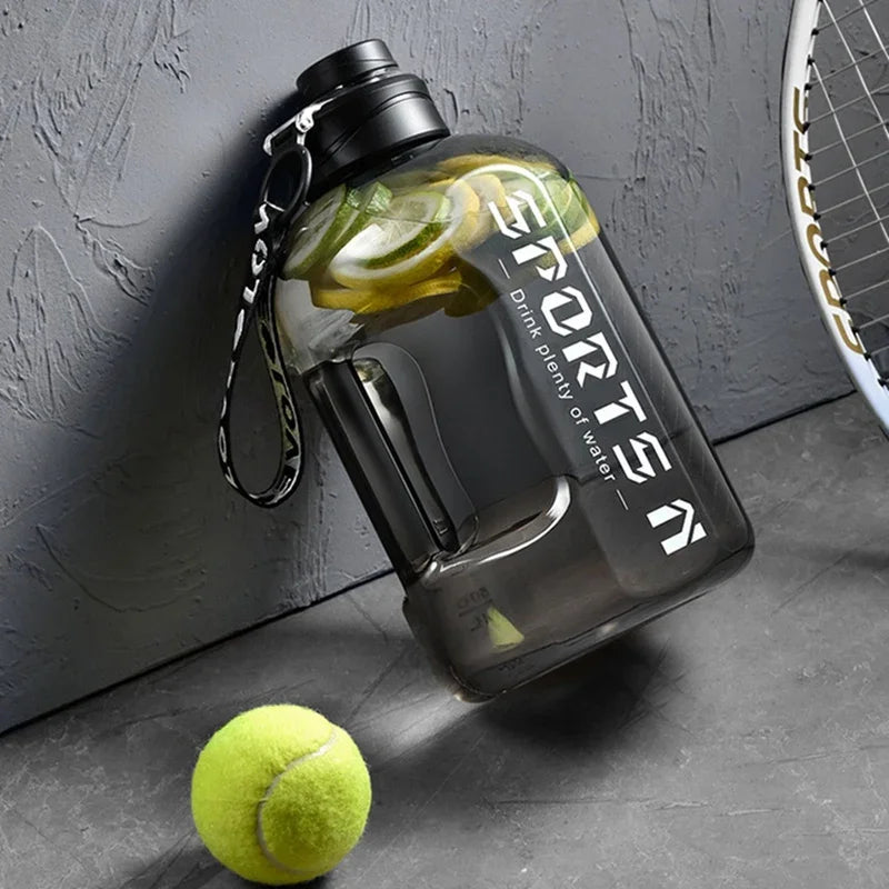 Klares Sportwasserflasche mit schwarzem Deckel und Limettenscheiben vor grauer Wand neben einem Tennisball.