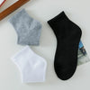 Eine Kollektion von drei Socken für den Knöchel in Grau, Weiß und Schwarz werden auf einer hellen Oberfläche präsentiert.