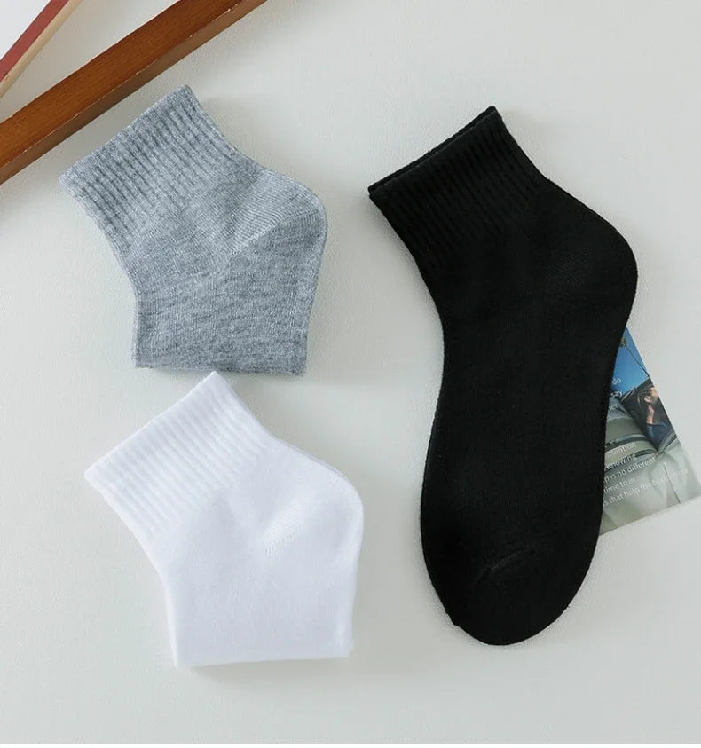 Eine Kollektion von drei Socken für den Knöchel in Grau, Weiß und Schwarz werden auf einer hellen Oberfläche präsentiert.