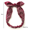 A deep maroon paisley patterned elastic hair headband tied in a bow.