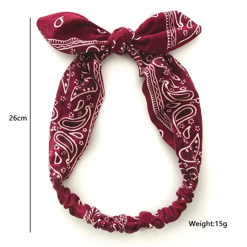 A deep maroon paisley patterned elastic hair headband tied in a bow.