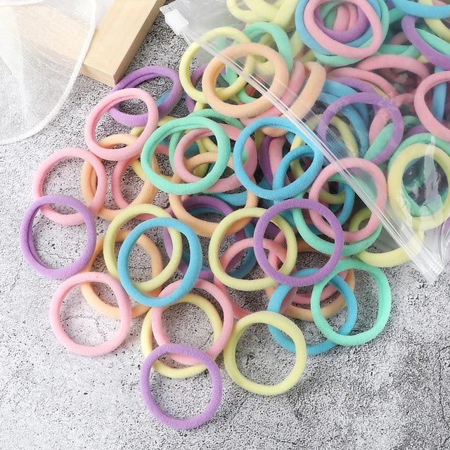 A pile of 50 mixed color elastic hair bands in various shades of pink, purple, green, and yellow on a gray surface.