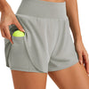 Person trägt graue, hochgeschnittene Sportshorts mit einer Tasche, die einen limengrünen Tennisball enthält.