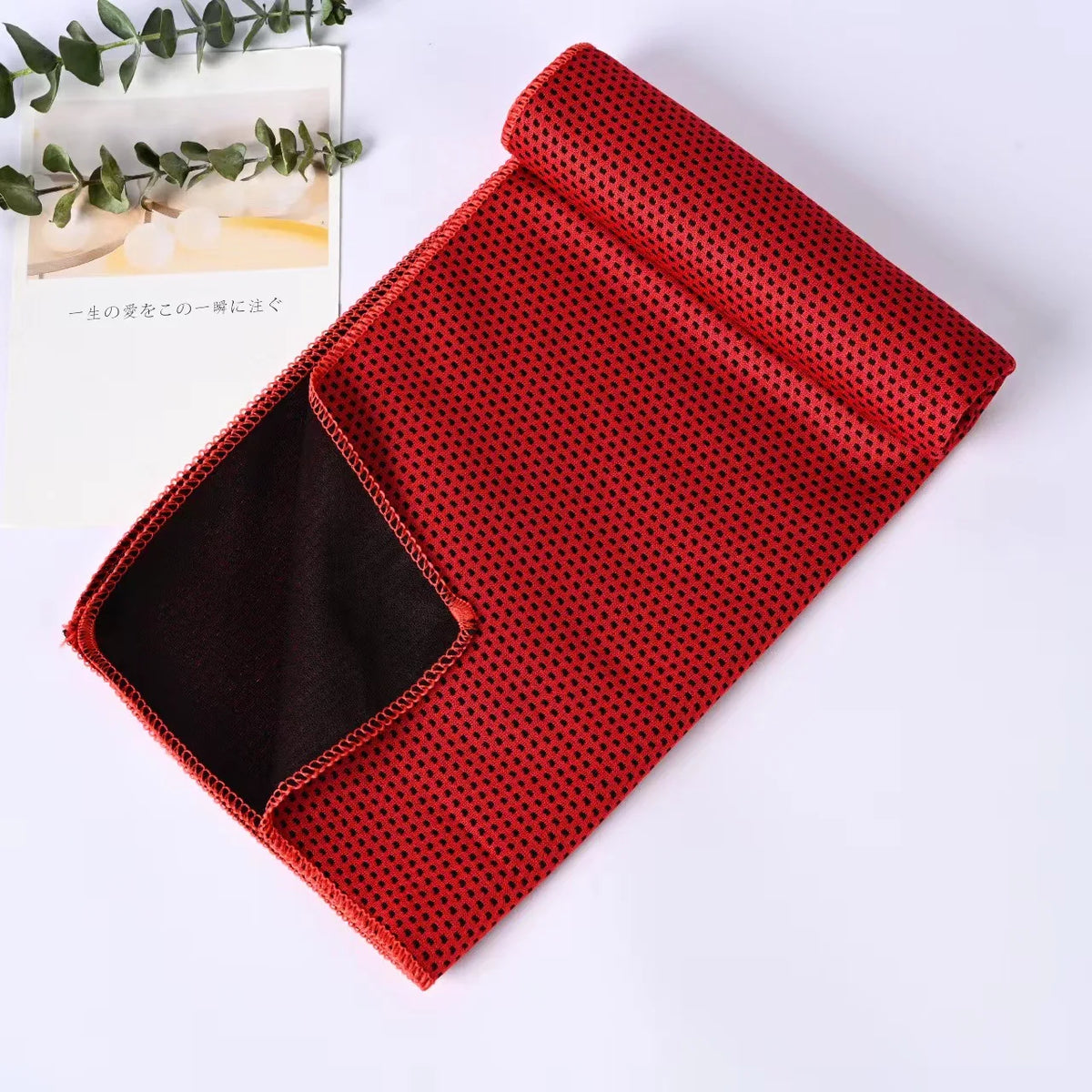 A red microfiber cooling towel with black trim is shown folded on a white surface.