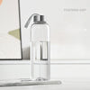 Una botella deportiva de agua transparente y a prueba de fugas con tapa plateada sobre una superficie blanca.