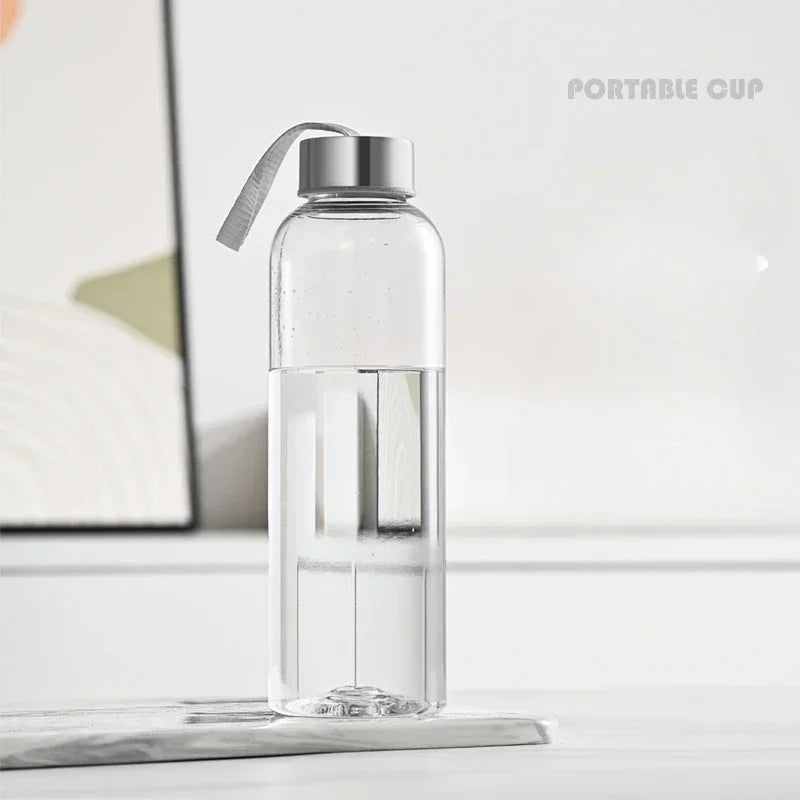 Una botella deportiva de agua transparente y a prueba de fugas con tapa plateada sobre una superficie blanca.