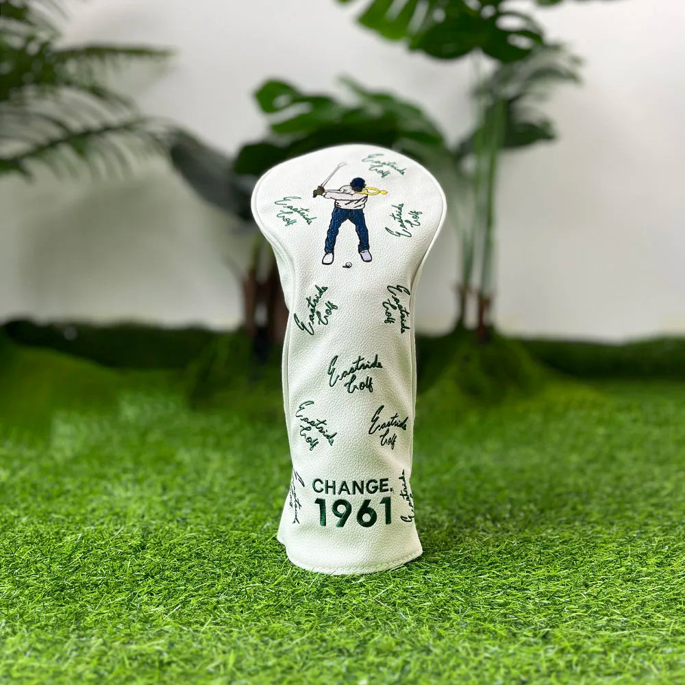 A white golf club head cover featuring a silhouette of a golfer and the year 1961 resting on green grass.