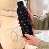 Una mano sostiene una taza de viaje de acero inoxidable aislante de doble pared negra con detalles de mariposa rosa contra un