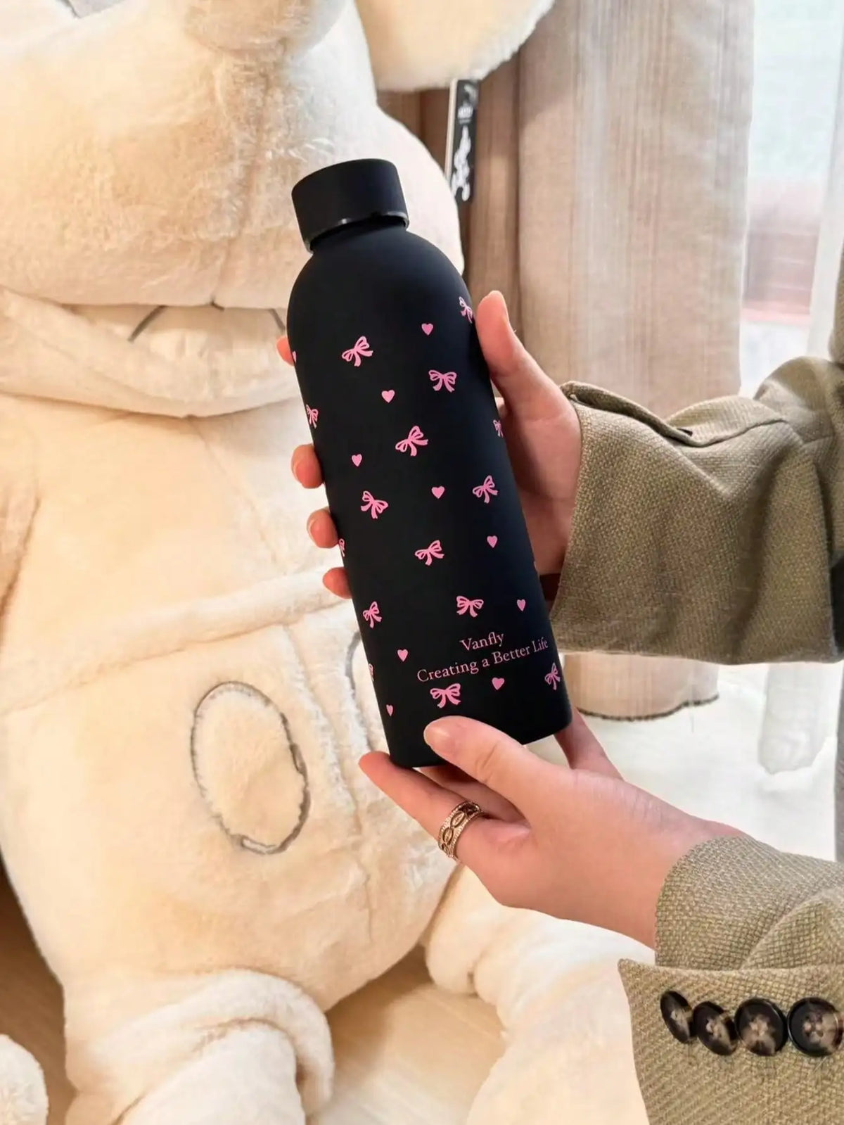 Una mano sostiene una taza de viaje de acero inoxidable aislante de doble pared negra con detalles de mariposa rosa contra un