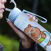 A person holds a cute capybara water bottle with a straw and handle against a blurred green background.