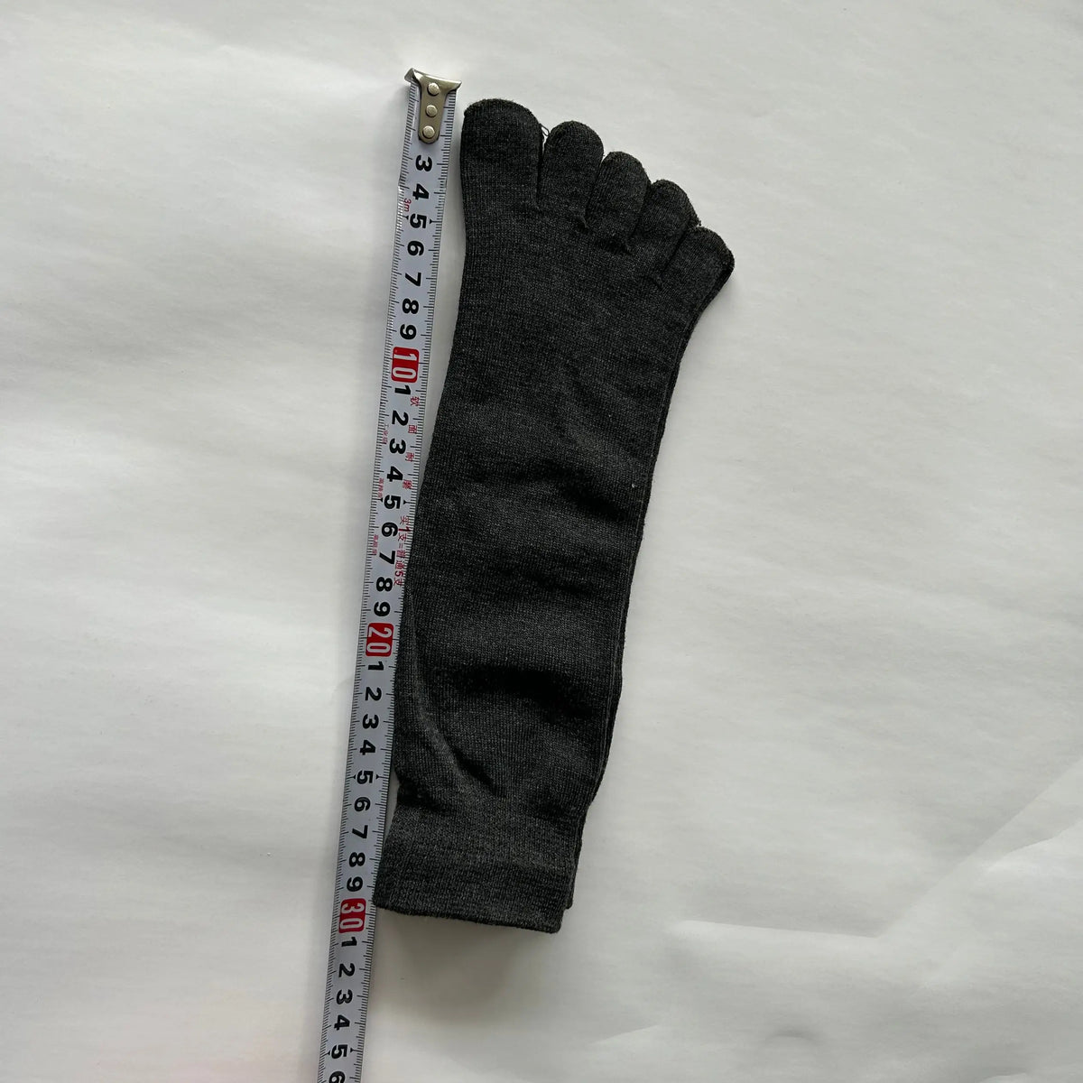 A gray men's breathable cotton split toe sock is shown next to a measuring tape.