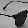 A close-up shot of black vintage square metal frame sunglasses resting on a light gray surface.