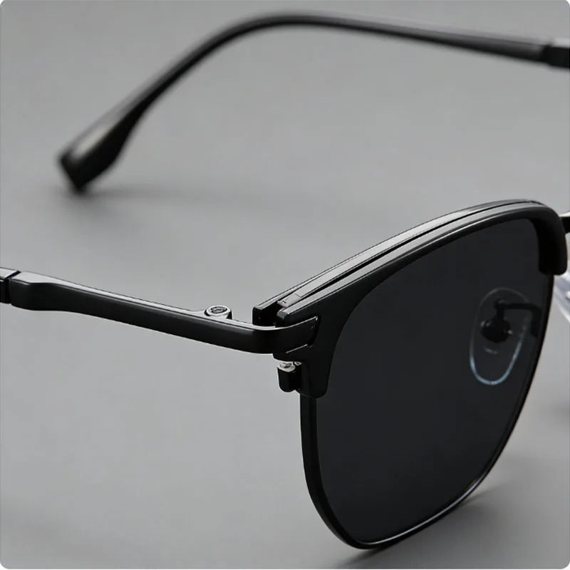 A close-up shot of black vintage square metal frame sunglasses resting on a light gray surface.
