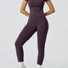 Eine Frau trägt ein lila Zweiteil-Yoga-Set mit hohen Bund-Leggings und einem kurzärmeligen Oberteil.