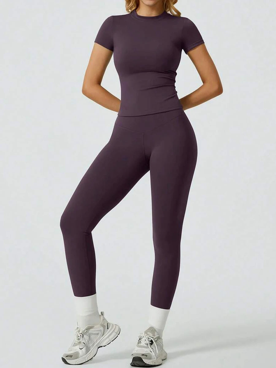 Eine Frau trägt ein lila Zweiteil-Yoga-Set mit hohen Bund-Leggings und einem kurzärmeligen Oberteil.