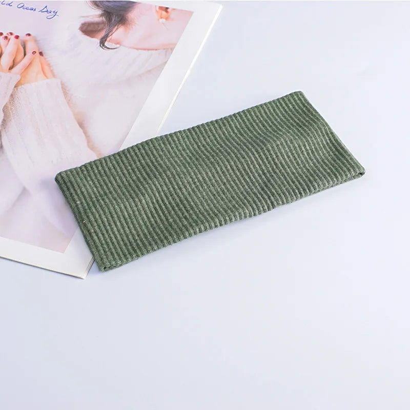 A close-up of a olive green ribbed knitted headband lying next to a magazine featuring hands.