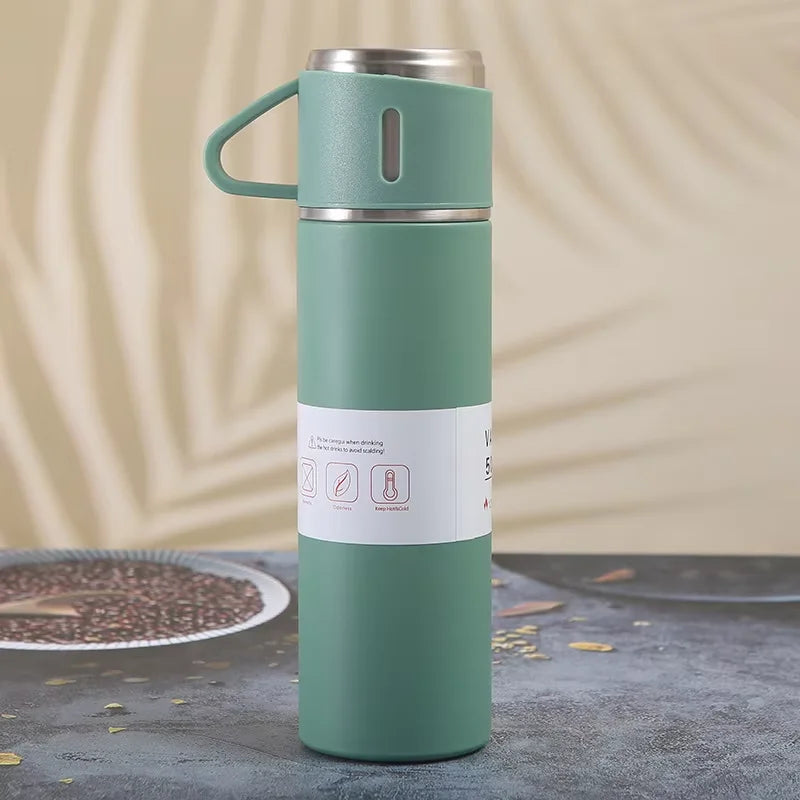 A tall, light green stainless steel vacuum flask with a handle is shown standing on a dark surface.