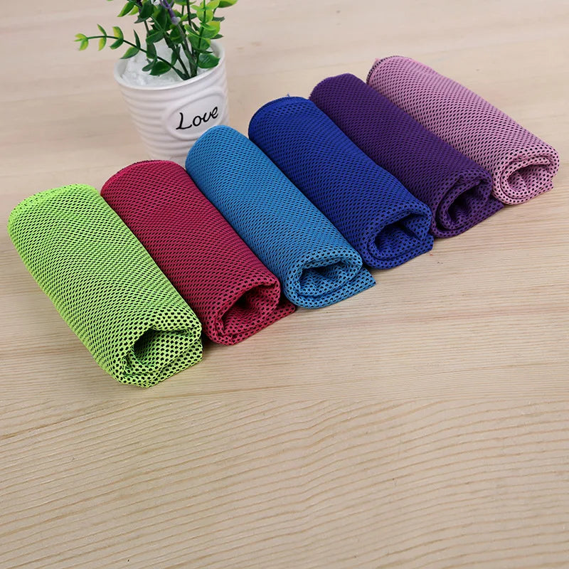 A collection of colorful microfiber cooling towels rolled up on a wooden surface.