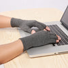 A hand wearing gray fingerless compression gloves is typing on a silver laptop computer.