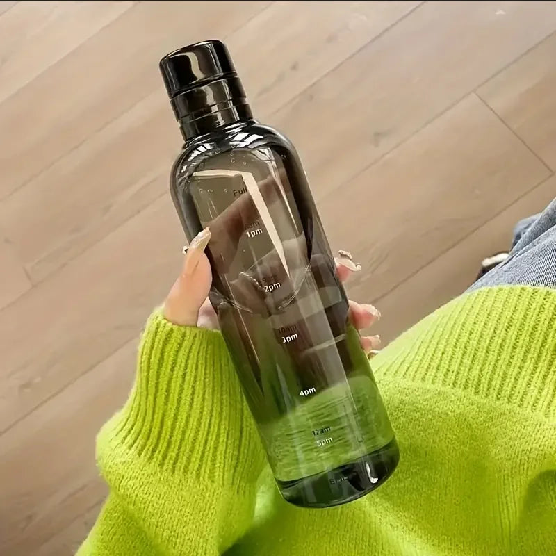 A hand holds a clear insulated water bottle with a time scale marked on it against a blurred wooden background.