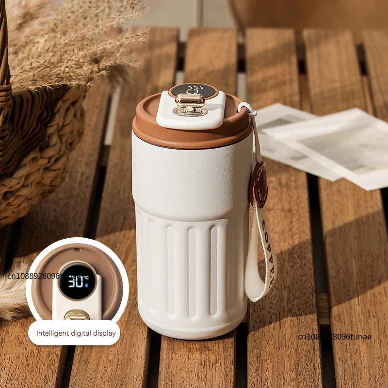 A white thermo mug with a brown lid and an intelligent digital display sits on a wooden surface.