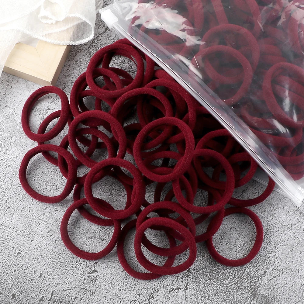 A pile of 50 elastic hair bands in various shades of red and maroon, some packaged in clear plastic.
