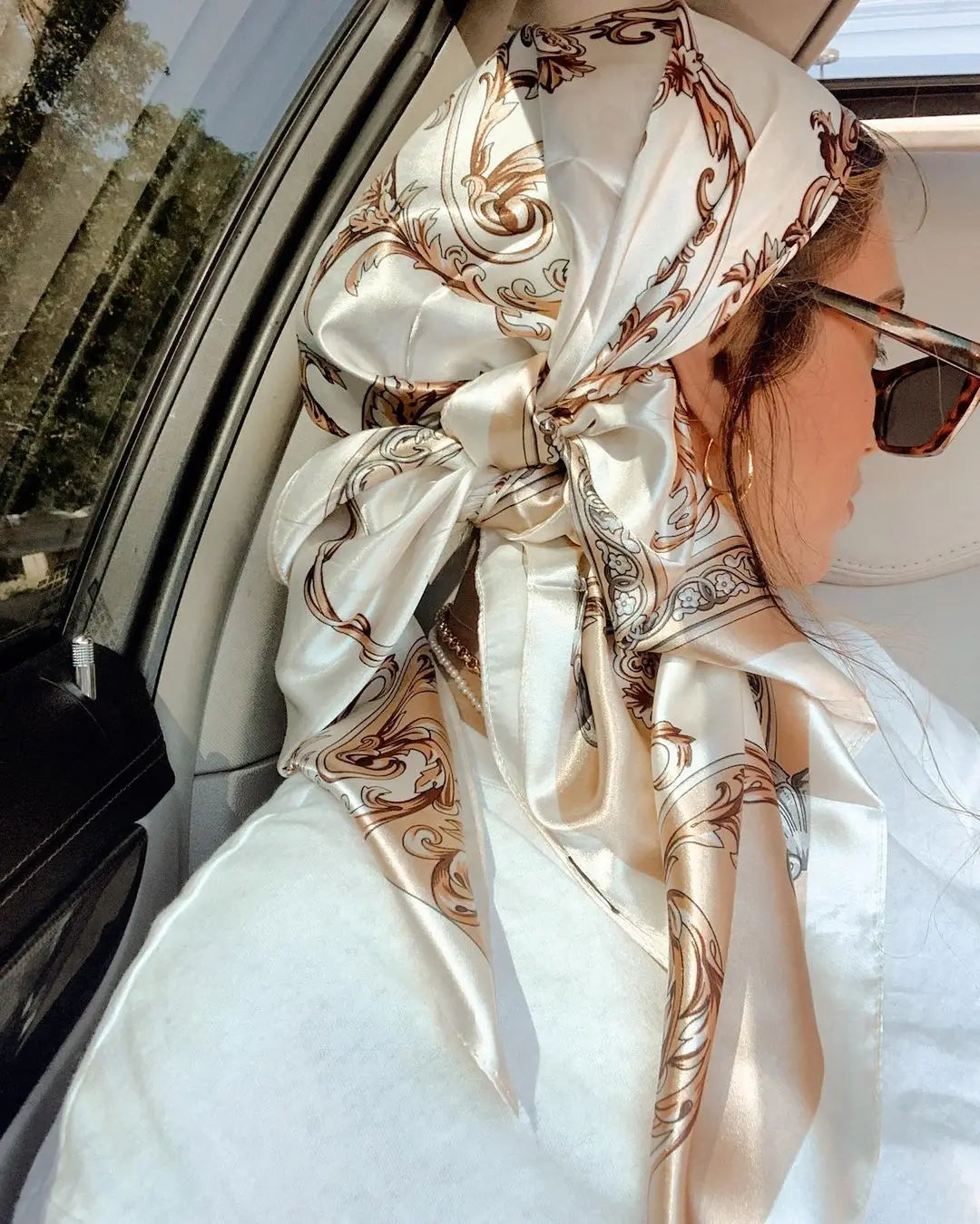 A close-up of a woman wearing an elegant satin square scarf tied in a voluminous bow for her hijab and hair.