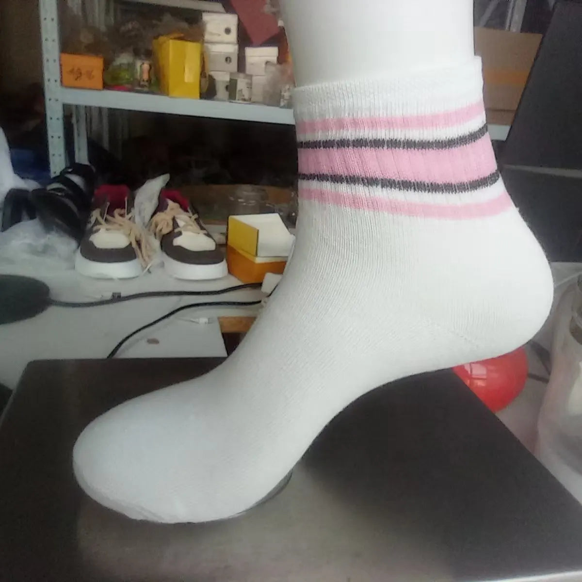 A close-up of a white sock with pink and black horizontal stripes, displayed on a dark surface.
