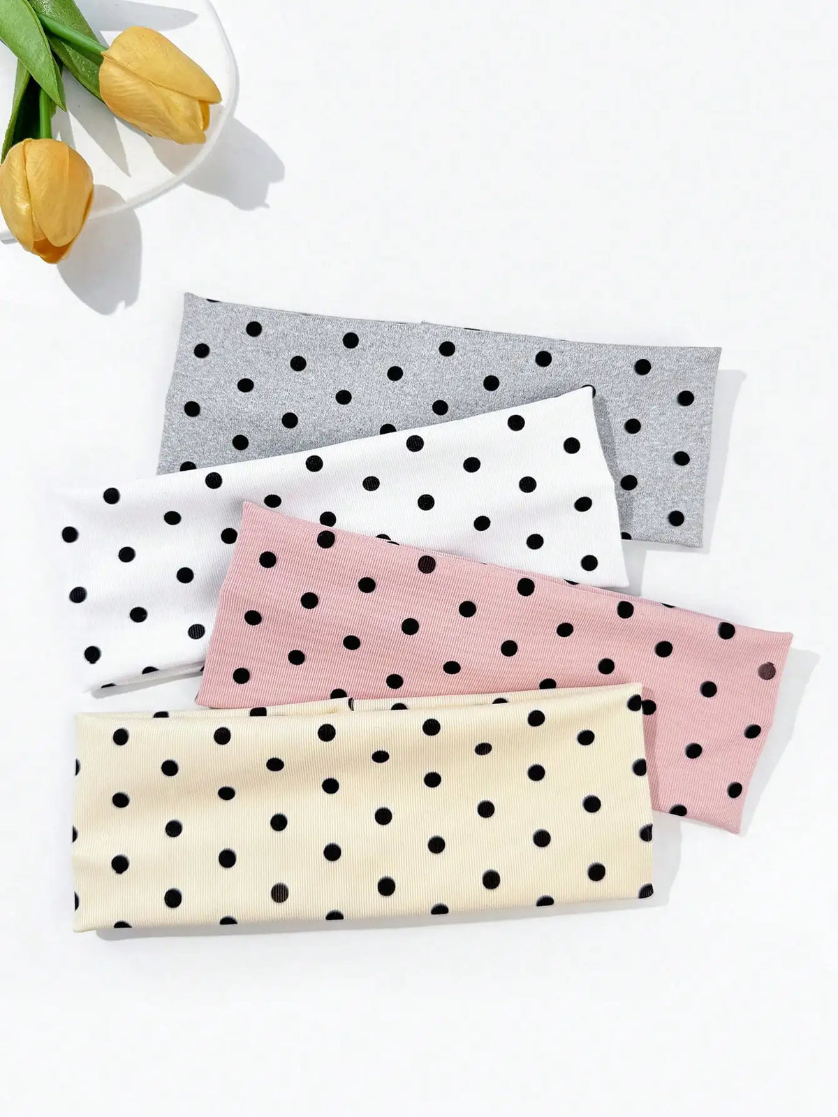 A set of four polka dot elastic hair bands in shades of pink, black, white, and gray are displayed on a white background.