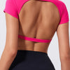A woman wearing a bright pink fitness crop top with a scoop back and black athletic bottoms.