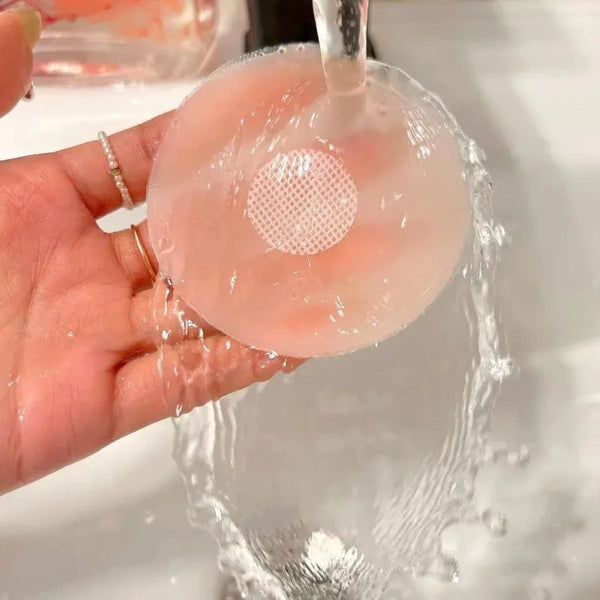 Eine Hand hält eine klare Silikon-Nippschutzhaube mit perforiertem Zentrum unter fließendem Wasser.