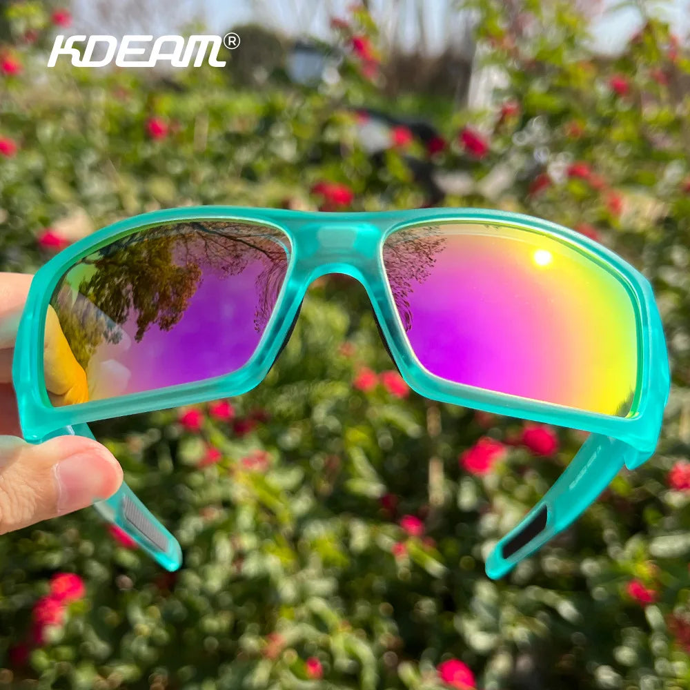 A pair of turquoise polarized sports sunglasses with mirrored lenses is held up against a blurred green background.