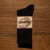 A black tube sock with a rectangular label featuring the word Quality in red text.