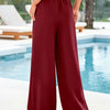 A model wearing maroon flowy high waist drawstring wide leg pants standing outdoors near a pool.